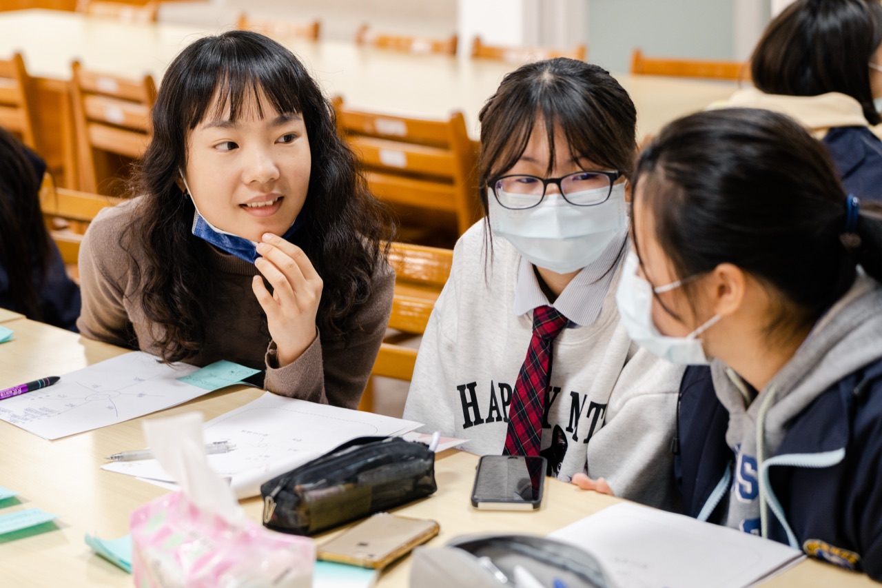三位學生在課桌前並肩討論、交換想法